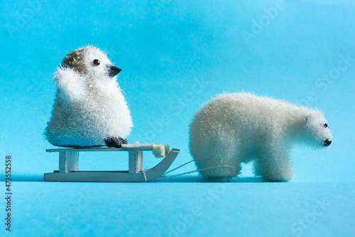 Winter background. Cute animals on a blue background. A polar bear and a penguin are sledding. photo