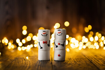 Marshmallow best friends. Two funny marshmallow snowmen. New year greeting card. Christmas winter holiday decoration. Christmas lights.