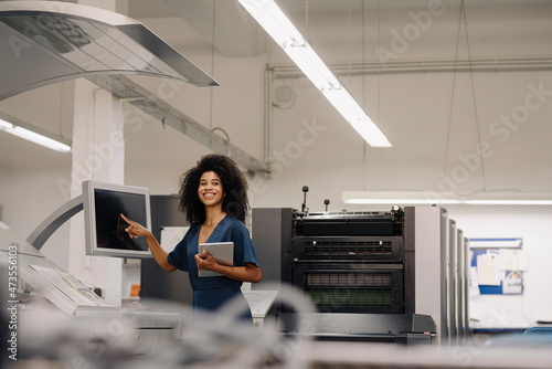 Smiling businesswoman with digital tablet looking away while pointing at device screen at industry