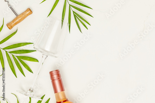 Drink composition with an empty wine glass, bottle of rose wine and palm leaves on a white background with copy space. The concept of a tropical holiday resort and relax. Summer party. Selective focus