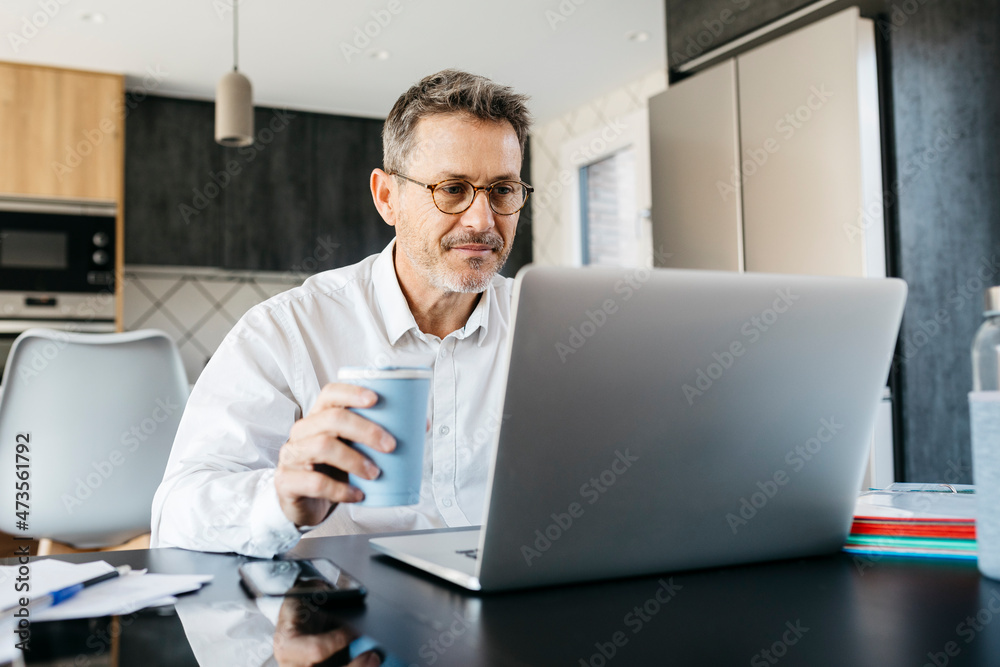 Businessman having coffee while working on laptop at home office Businessman having coffee while working on laptop at home office
