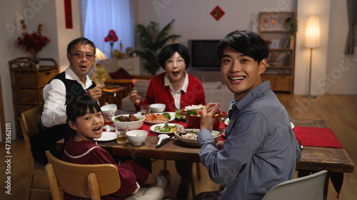 slow motion of happy family at dinner table turning head and look at camera in surprise as someone is serving the main dish for reunion meal at home