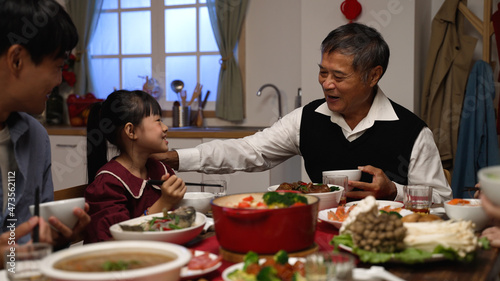smiling senior man grandfather talking with hand gestures as the girl granddaughter giving food to him at the family reunion dinner party on the eve of Chinese new year