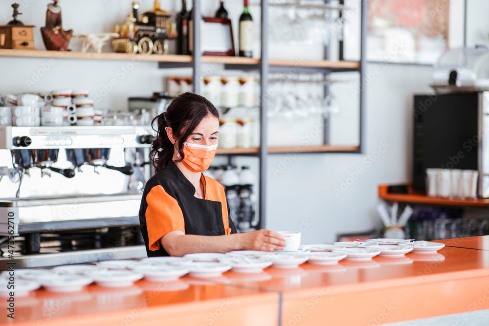 Waitress wearing protective face mask arranging cup on saucer at cafeteria counter Waitress wearing protective face mask arranging cup on saucer at cafeteria counter