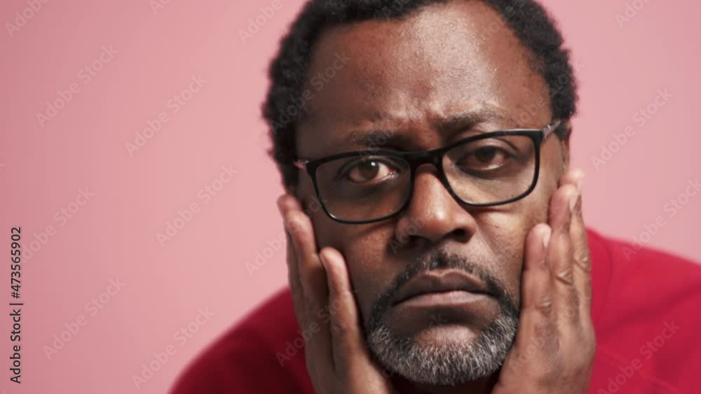 Concentrated adult African man correcting his appearance at the camera in the pink studio