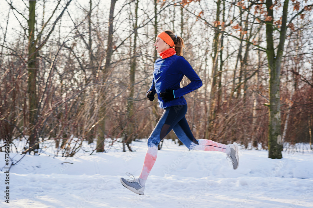 Woman running near bare trees during snow in winter Woman running near bare trees during snow in winter