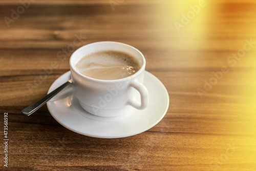 A cup of hot coffee on a saucer with a spoon stands on a wooden background of a table in a cafe
