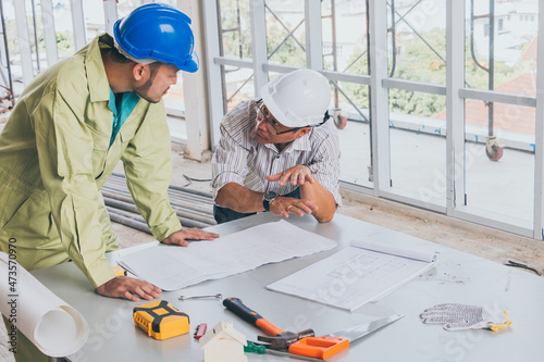 Engineer and worker looking home plans with helmet, craftsman tool and home model on workplace at construction site.