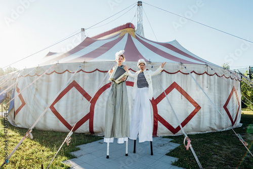 Female artists playing accordion while standing on stilts by male circus performer photo