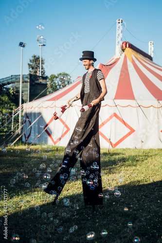 Male juggler holding juggling pins while walking with stilts on meadow