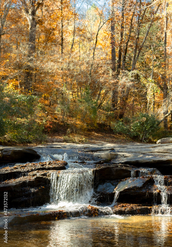 A vertical shot of a small waterfall over rocks in the autumn woods.