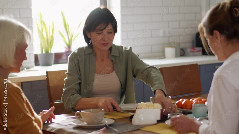 Concentrated mature women cuts cake and drinking tea at home