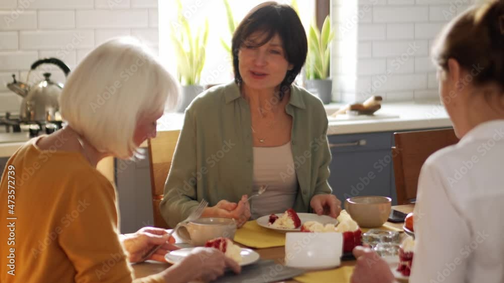 Positive mature women eating cake and talking at home Positive mature women eating cake and talking at home