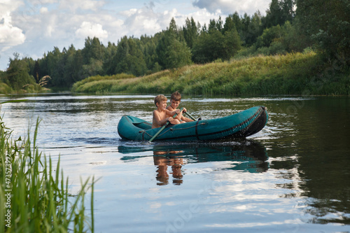 Two children ride a rubber boat on the river on a summer day.