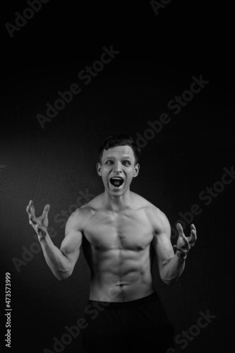 Black and white portrait athletic man screams emotionally on a black background.