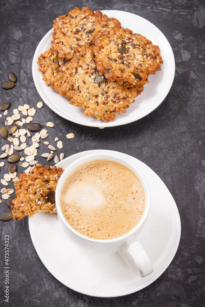 Cup of coffee with milk and homemade oatmeal cookies on white plate. Delicious crunchy dessert Cup of coffee with milk and homemade oatmeal cookies on white plate. Delicious crunchy dessert