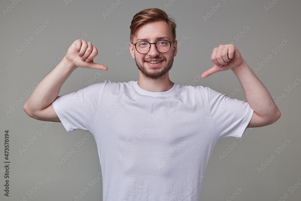 Studio portrait of young bearded man, wears casually posing over gray studio background points with a finger at himself, smiles broadly with happy facial expression. isolated. Studio portrait of young bearded man, wears casually posing over gray studio background points with a finger at himself, smiles broadly with happy facial expression. isolated.