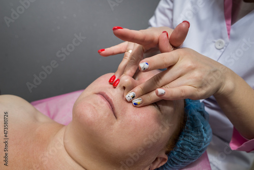 The beautician massages the face and head of an adult woman lying on a massage table.