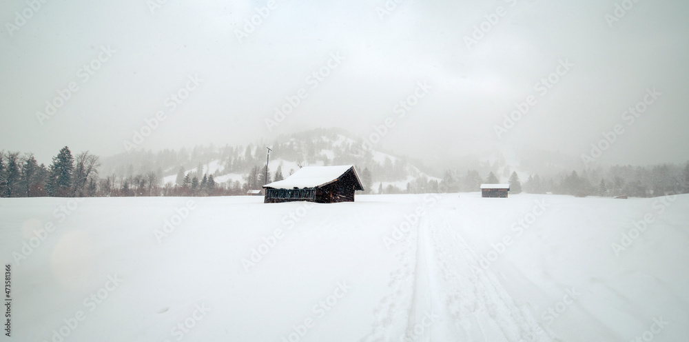 Kalte und verschneite Winterlandschaft auf einer Alm mit Almhütten in den bayerischen Alpen an einem stürmischen Schneetag 