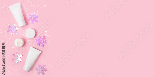 Composition from blank cosmetics containers and glittering snowflakes on the pink background with snow.Good for text overlay,winer sales and offers,large banner. © Bidzilya