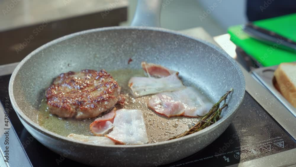 Close up of chef grilling burger meat and bacon on heated pan among oil, garlic and rosemary. Cooking of delicious fast food at restaurant. Close up of chef grilling burger meat and bacon on heated pan among oil, garlic and rosemary. Cooking of delicious fast food at restaurant.