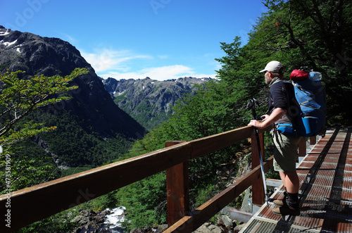 Man with big backpack standing on bridge with green mountain view in Nahuel Huapi national park, Hiking in Patagonia, Argentina