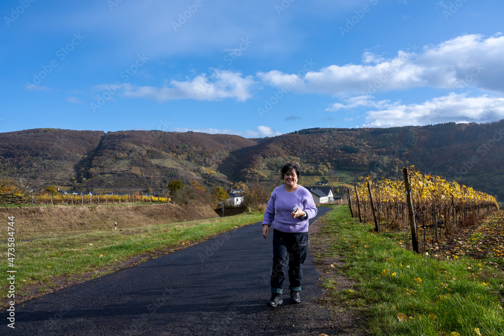 A woman on a road going through a wine district n the Mosel valley. Beautiful yellow vine leaves and green grass against a blue sky
