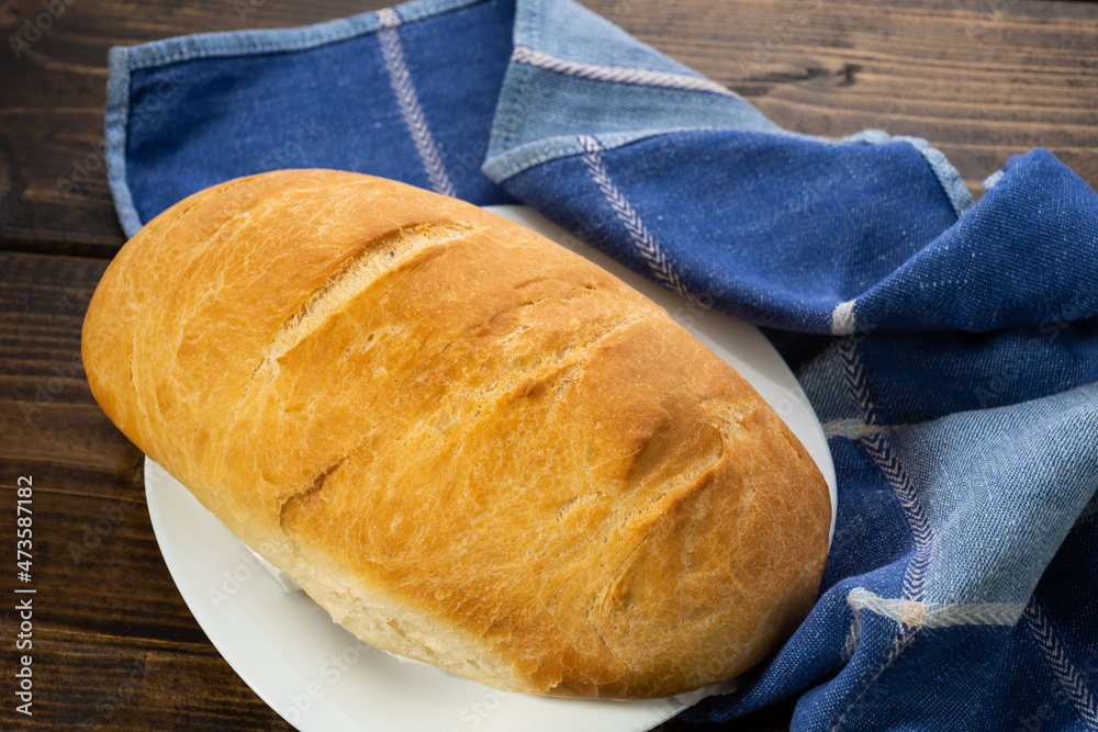 fresh baked loaves of bread on lie on a dark wooden table next to a blue towel rag