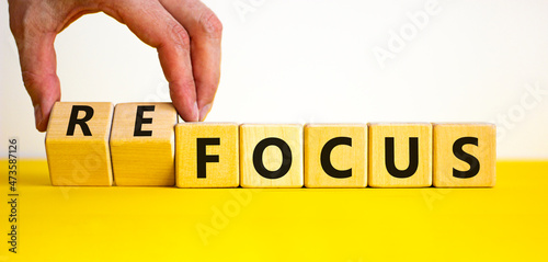 Focus or refocus symbol. Businessman turns wooden cubes and changes the word focus to refocus. Beautiful yellow table white background, copy space. Business, focus or refocus concept. photo