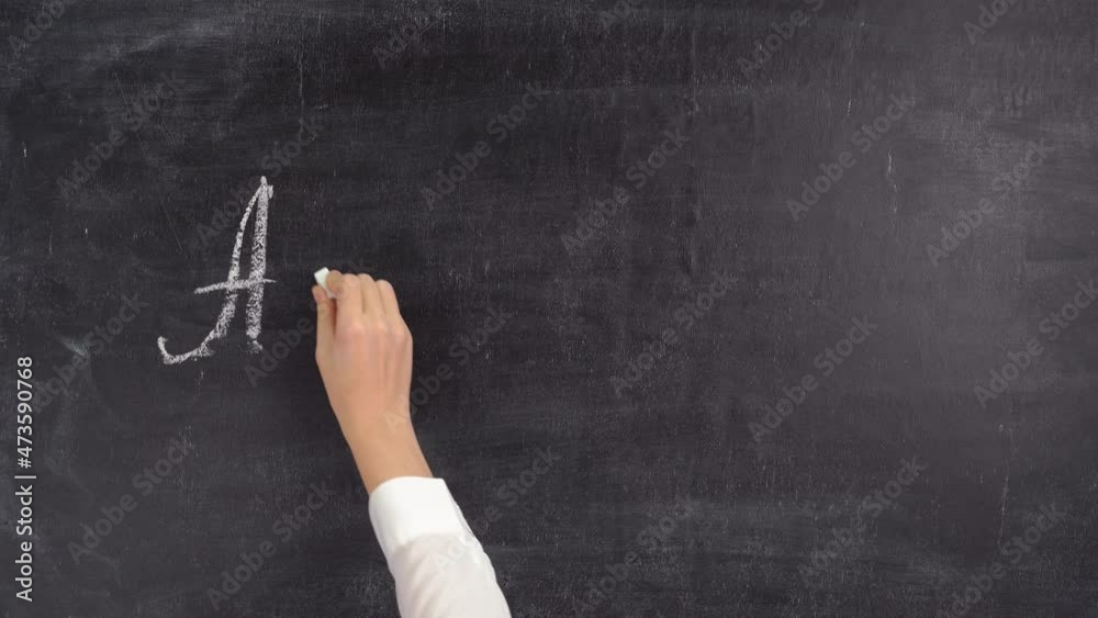 The teacher writes letters of the English alphabet on a chalkboard. The concept of learning English