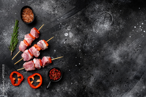 Marinated raw kebab on skewers, top view flat lay, with copy space for text, on black dark stone table background