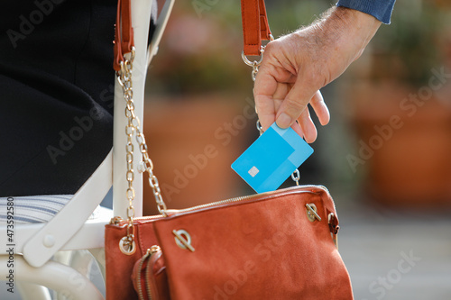 Man's hand stealing a credit card from a purse in a restaurant terrace outdoors