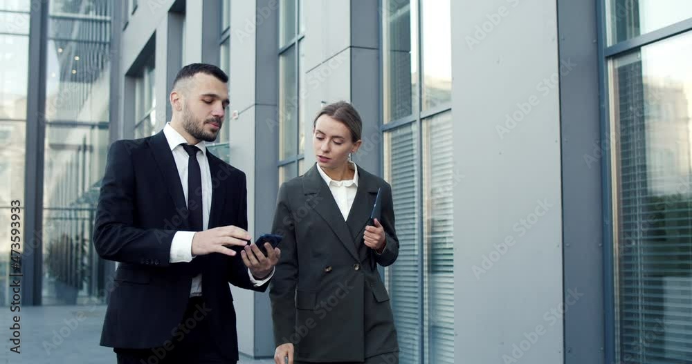Caucasian businessman and businesswoman looking at the tablet screen while working outdoor the office in the city Caucasian businessman and businesswoman looking at the tablet screen while working outdoor the office in the city