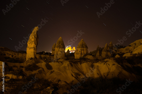 Long exposure night shot of ancient cave houses near Goreme and city lights in the background. Popular travel destination in Turkey. UNESCO World Heritage Site