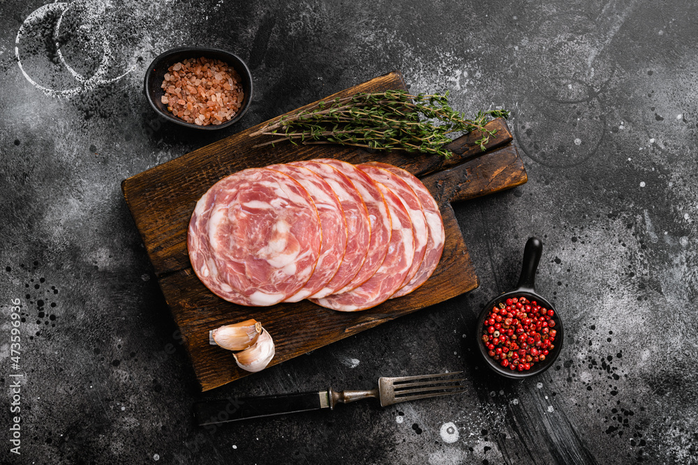Sliced raw smoked sausage, on black dark stone table background, top view flat lay, with copy space for text