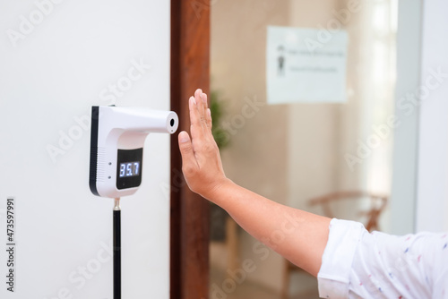 Closeup woman lifts her hand at the temperature meter in front of the coffee shop, primary screening by checking the body heat before getting into to the shop during covid-19 pandemic
