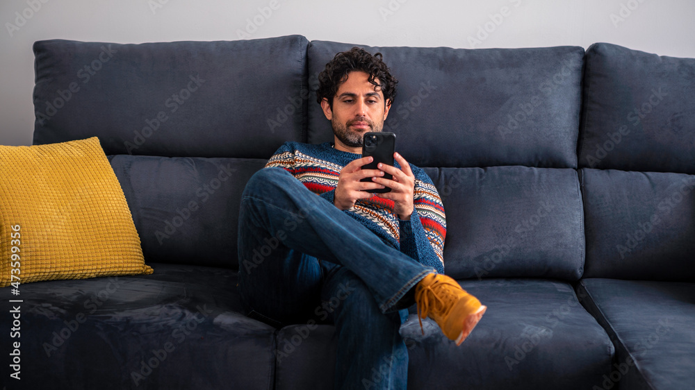 Fototapeta premium Portrait of caucasian man using smartphone sitting on couch at beautiful house