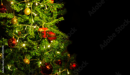 Close up of decorations on a Christmas tree with lights on. Selective focus and black background.