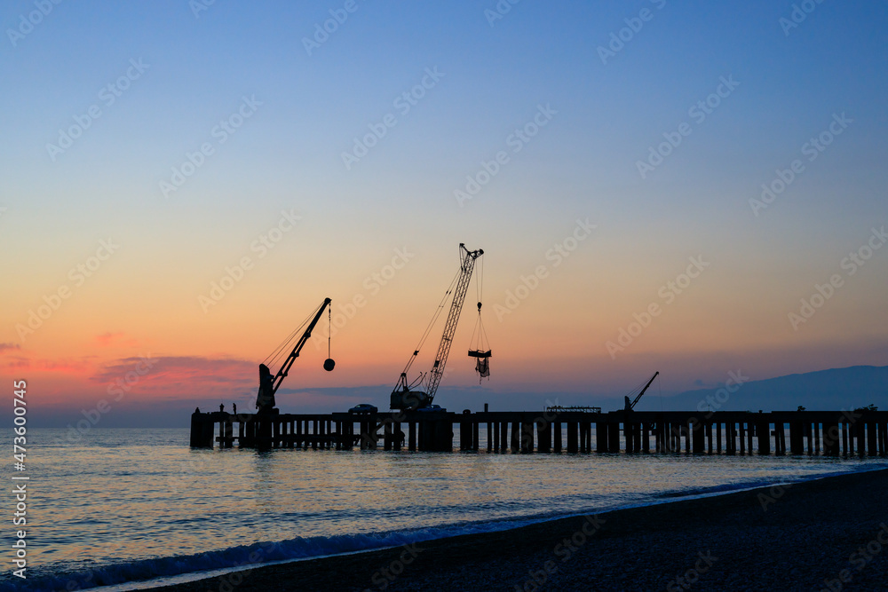 beautiful sunset on the sea, silhouette of the old pier with cranes