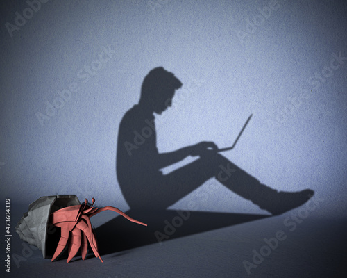 The concept of dependence of people on gadgets, the Internet. A paper figure of a hermit crab that casts a shadow on a guy sitting behind a laptop. 3d illustration. photo