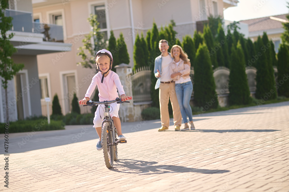 Fototapeta premium A girl riding a bike while her parents watching her