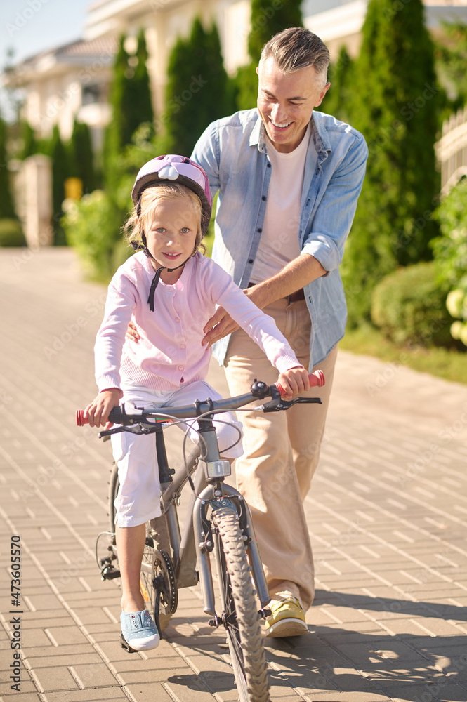 A man supporting a girl while she riding a bike A man supporting a girl while she riding a bike
