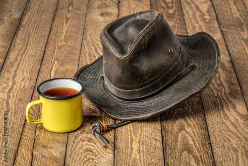 weathered outback oilskin hat with metal enamel mug of tea on a rustic wooden table