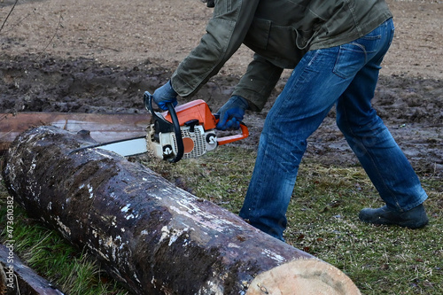 man holds chainsaw and saws log. The chain saw is in motion. Production of log cabins. Deforestation. Sawing wood