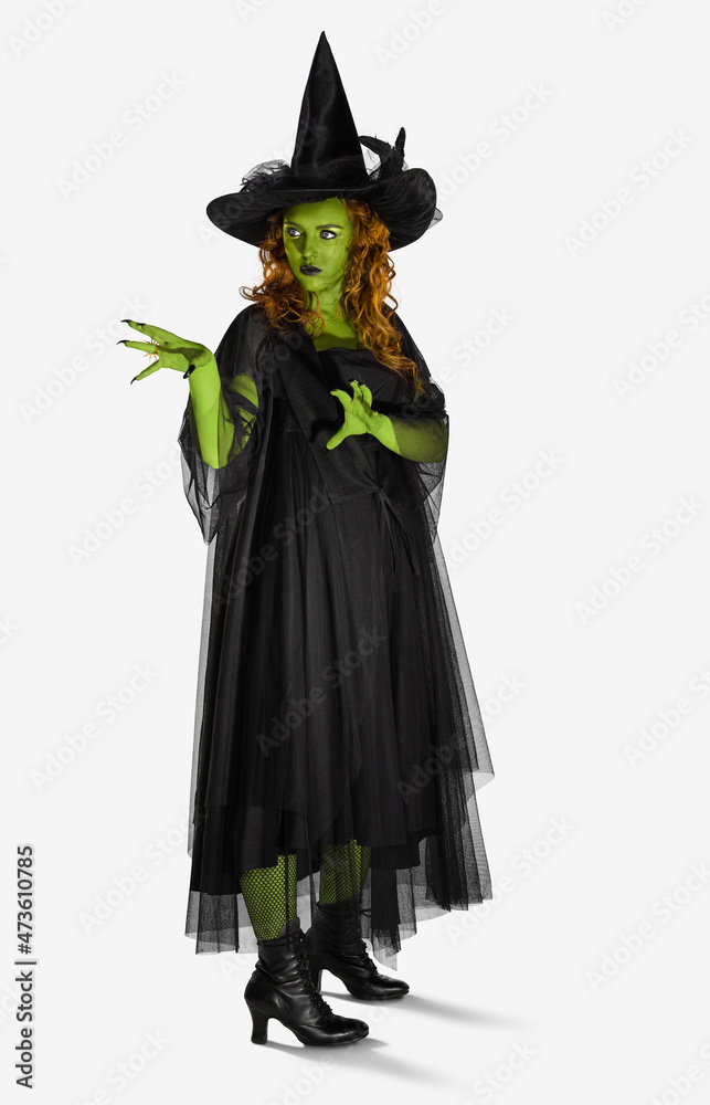 Portrait of a woman dressed as a witch against a white background with green body paint, looking off camera with her hands up casting a spell. Portrait of a woman dressed as a witch against a white background with green body paint, looking off camera with her hands up casting a spell.