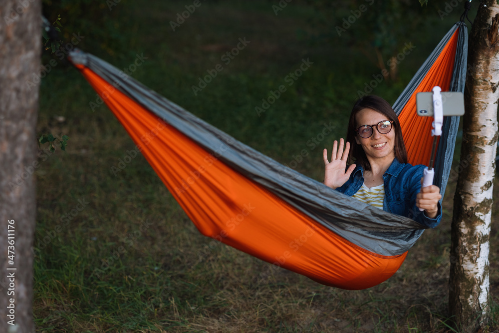 a European woman in a hammock in nature speaks via video link with a webcam. a female travel blogger creates video content. hiking and outdoor recreation on the seashore or in the forest. a cozy a European woman in a hammock in nature speaks via video link with a webcam. a female travel blogger creates video content. hiking and outdoor recreation on the seashore or in the forest. a cozy