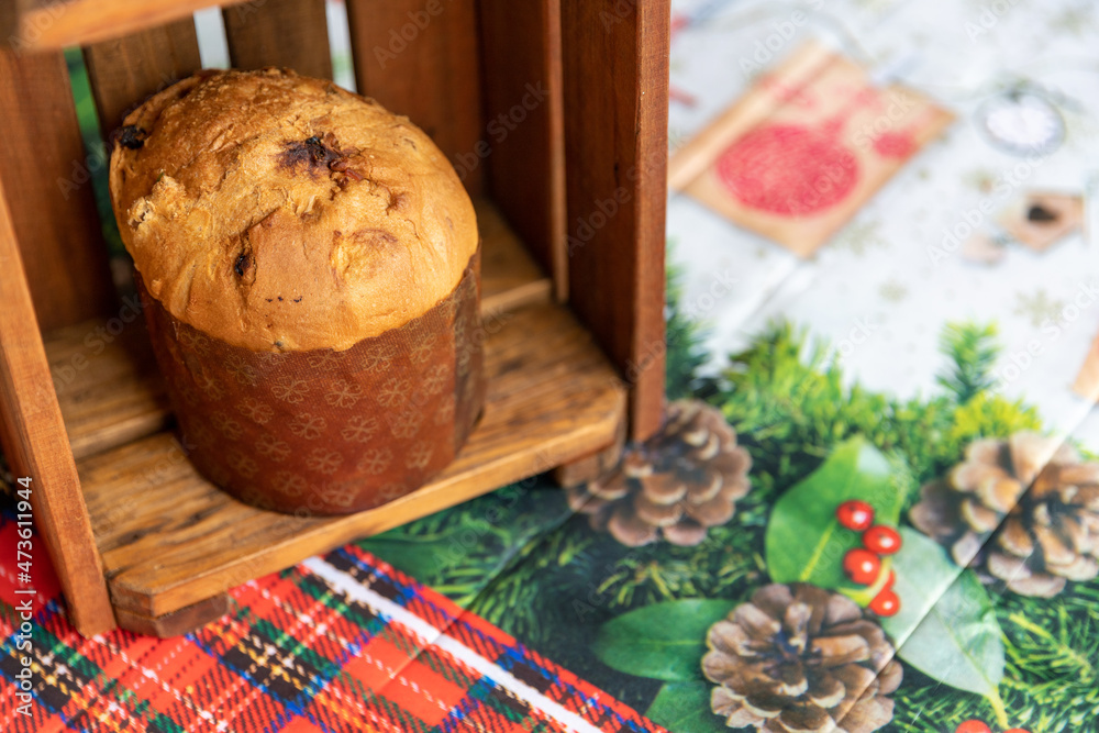 Panettone in wooden box on table with Christmas tablecloth.