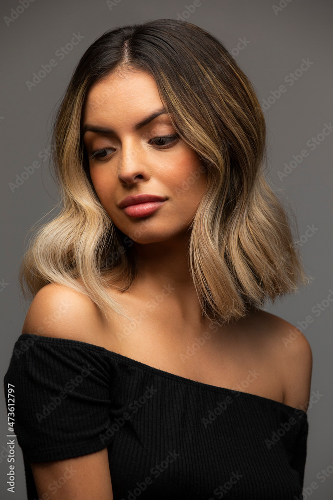 Portrait of Hispanic woman wearing off the shoulder top on gray background, looking down off camera Portrait of Hispanic woman wearing off the shoulder top on gray background, looking down off camera
