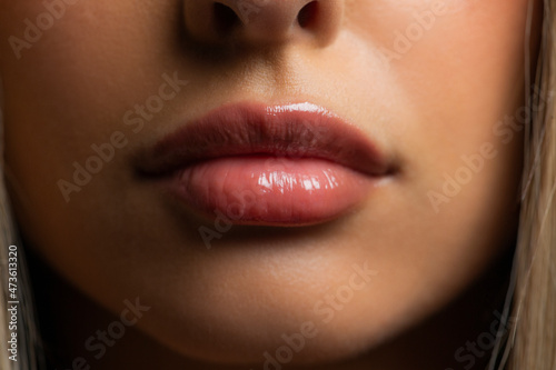 Straight on shot of a young womans lips, wearing glossy lipstick