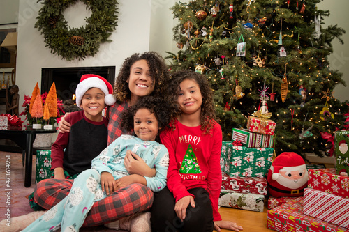 Mother sitting with her three children smiling at camera in front of Christmas tree.  photo